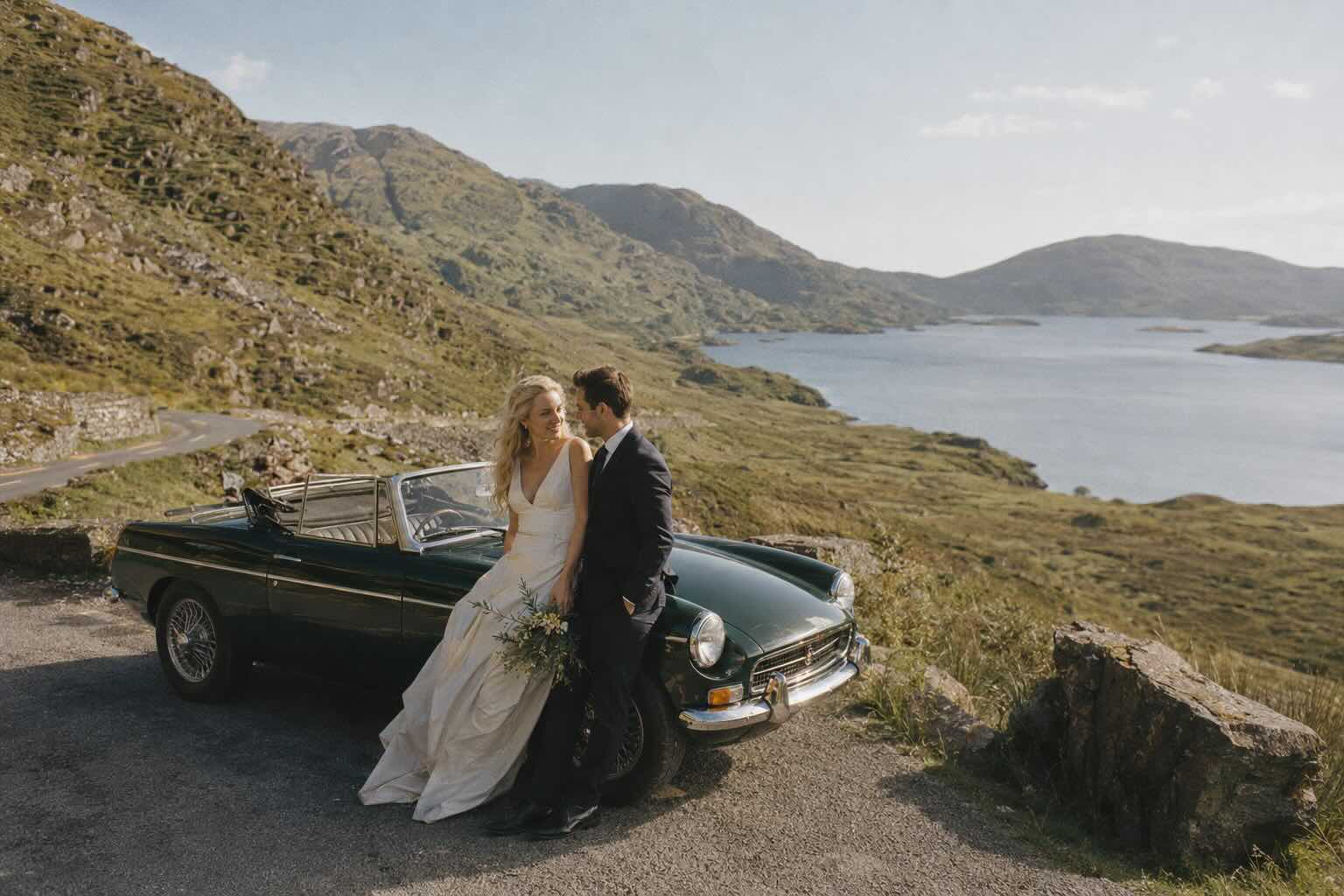 bride and groom sitting on car by a lake